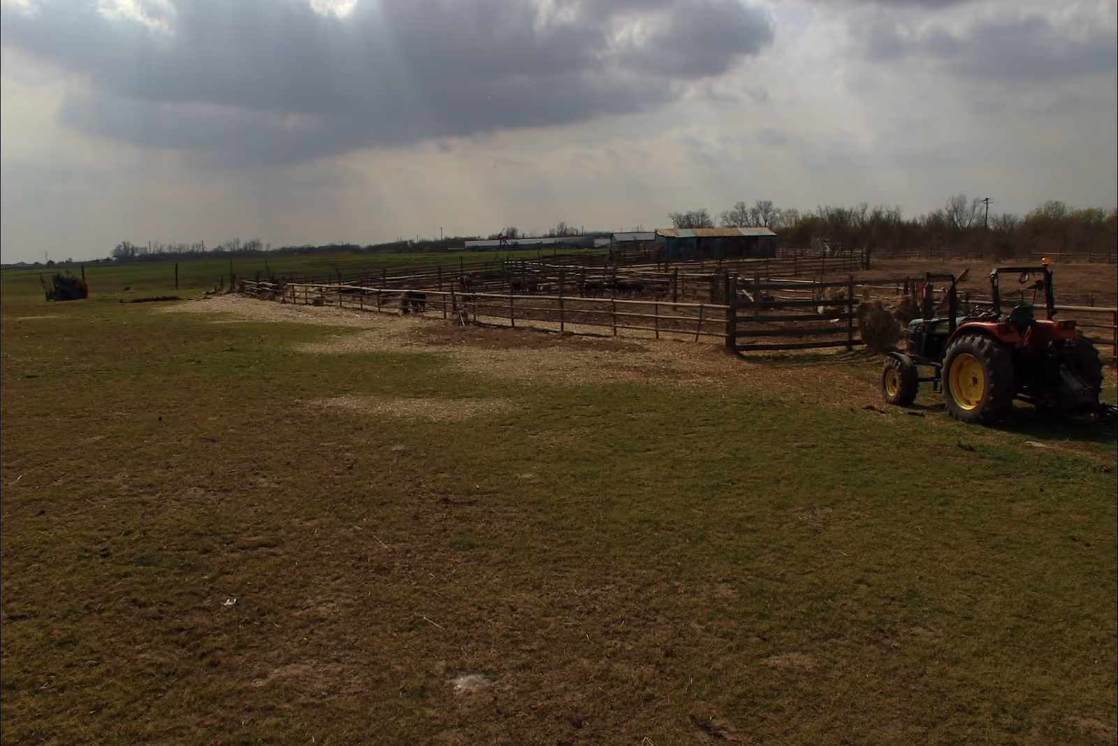 Practical tractor beside cattle pens beneath a changing Kansas sky